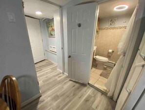 A hallway with a wooden floor leading to a bathroom with a toilet and shower.