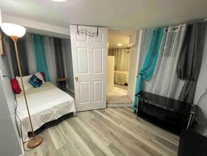 A bedroom with a bed, a floor lamp, a TV, and a door leading to another room.