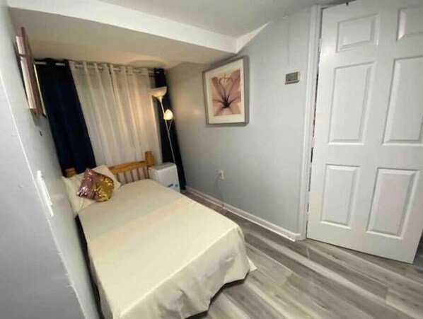 Un dormitorio con una cama, una mesita de noche, una lámpara, una puerta y un cuadro en la pared.
