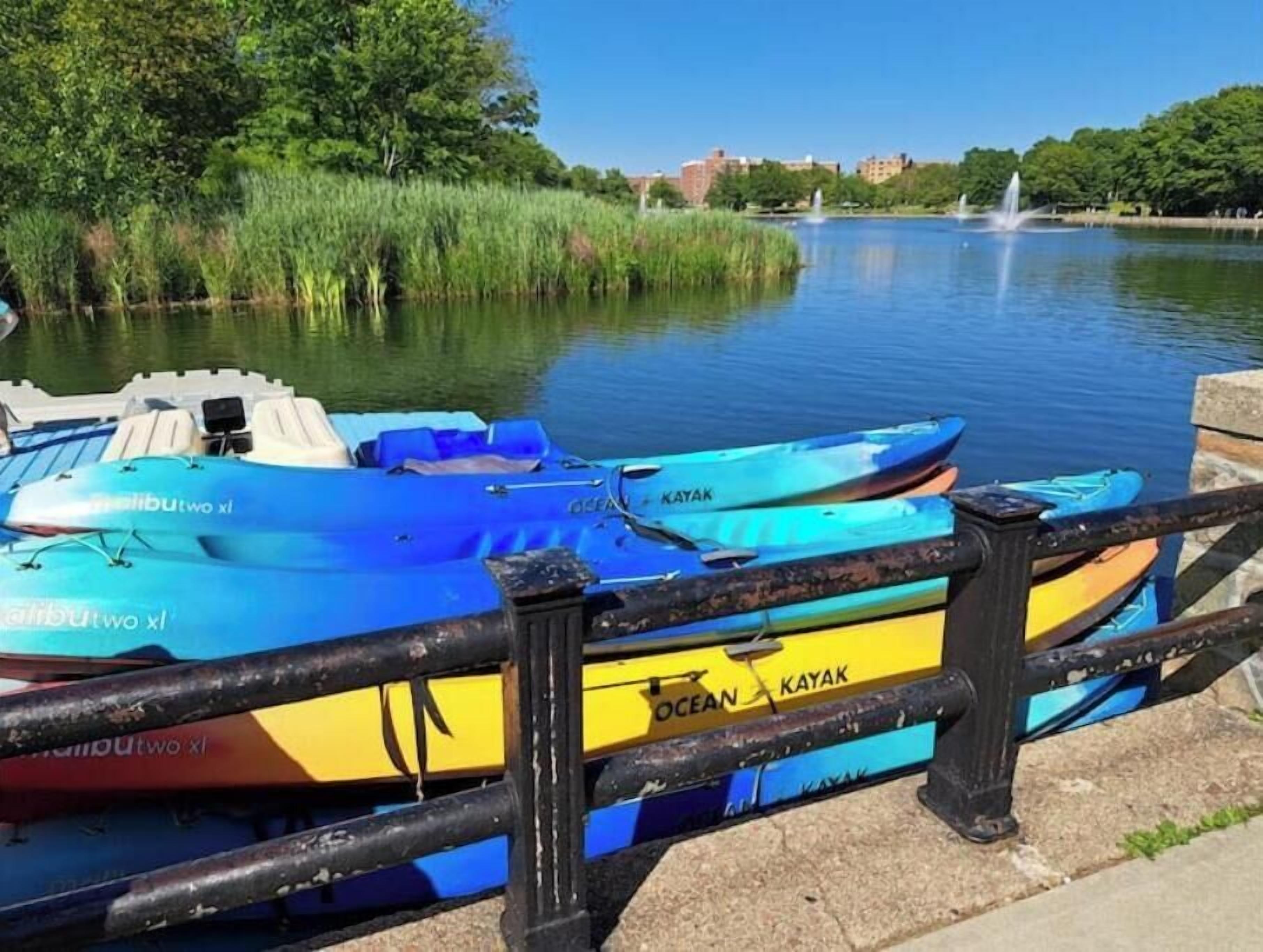 A row of blue and yellow kayaks docked at a pier with a cityscape in the background.