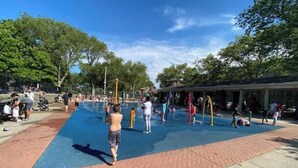 Een openbaar zwembad met een blauw wateroppervlak, omgeven door een betegelde looppad en bomen.