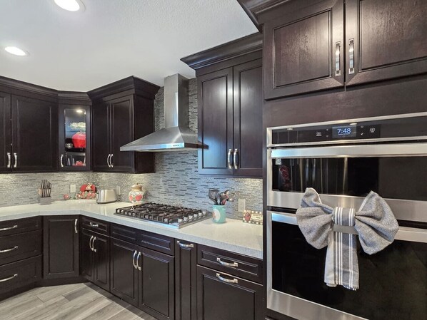 A modern kitchen with dark wood cabinets, a stainless steel range hood, a built-in oven, and a clock displaying 7:48.