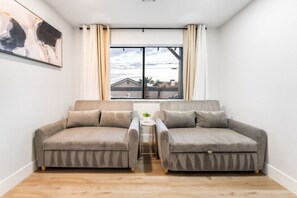 Une pièce avec deux canapés gris, une petite table sur laquelle est posée une plante, et une fenêtre avec des rideaux.