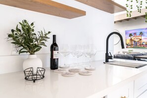 Eine moderne Küche mit weißer Arbeitsplatte, einem Blumentopf, einer Weinflasche und Weingläsern.
