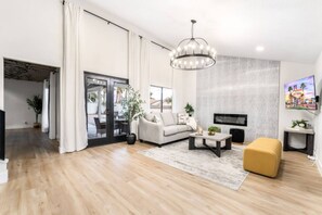 A modern living room with a sofa, coffee table, and ottoman. There is a television mounted on the wall and a chandelier hanging from the ceiling. - LUX 5BR | 2 Master BR | 2 Living Rooms |Pool & Spa (Las Vegas)