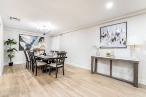 Un comedor con una mesa y sillas de madera, una planta en maceta y un cuadro en la pared.