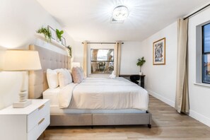 A modern bedroom with a large bed, bedside tables, a desk, and a view of the outdoors.