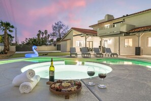 Una piscina con sillas de descanso y una decoración de cisne, un jacuzzi con copas de vino y una botella, y un cuenco con aperitivos.