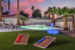 Un jardin avec une piscine, des chaises longues et un cygne gonflable bleu.