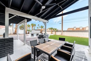 An outdoor patio with a covered seating area, a barbecue grill, and a pool in the background.