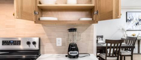 Une cuisine moderne dotée d’une cuisinière intégrée, d’un mixeur posé sur le plan de travail, de meubles de rangement en bois et d’un coin repas avec des chaises et une table.