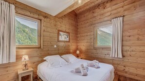 Camera da letto in una baita di legno, con un letto, due lampade sui comodini e un quadro appeso al muro.