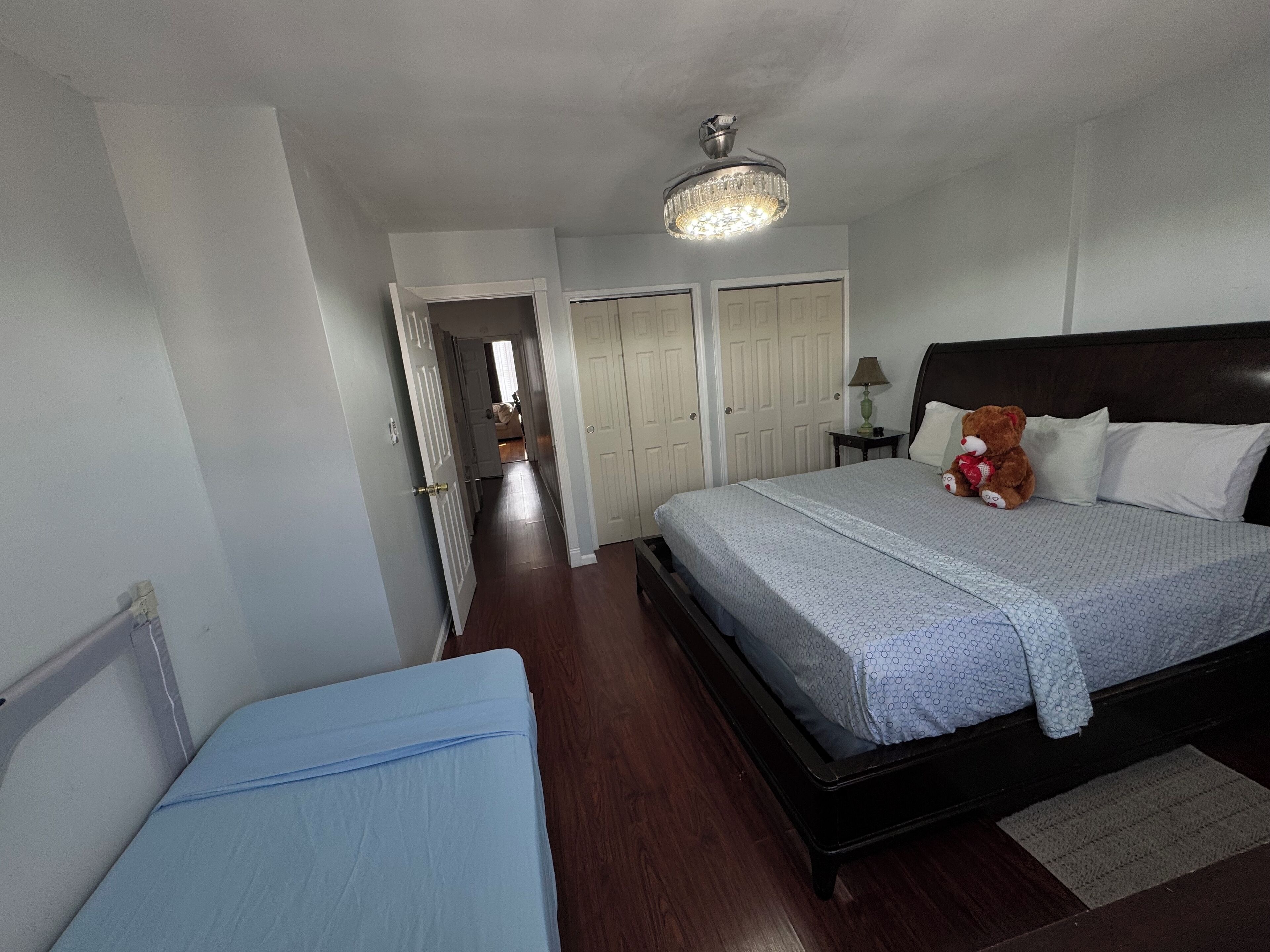 Une chambre à coucher avec un lit, une table de chevet, un ours en peluche et un luminaire au plafond.