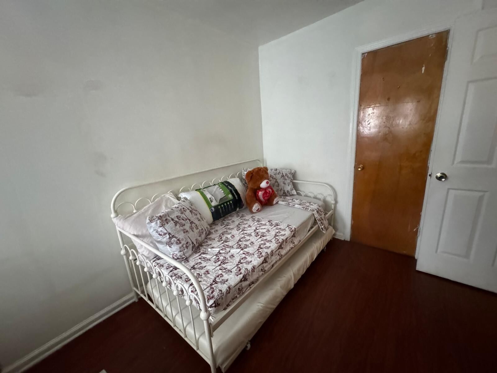 A small, white metal bed with floral bedding and a teddy bear.