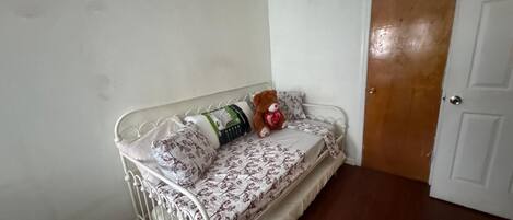 A small, white metal bed with floral bedding and a teddy bear.