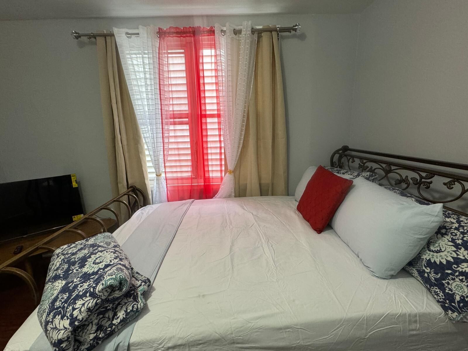 A bedroom with a bed, curtains, a TV, and a metal bed frame.