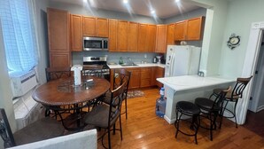 A kitchen with wooden cabinets, a stainless steel microwave, a stove, and a refrigerator. There is a dining table with chairs and a water dispenser.