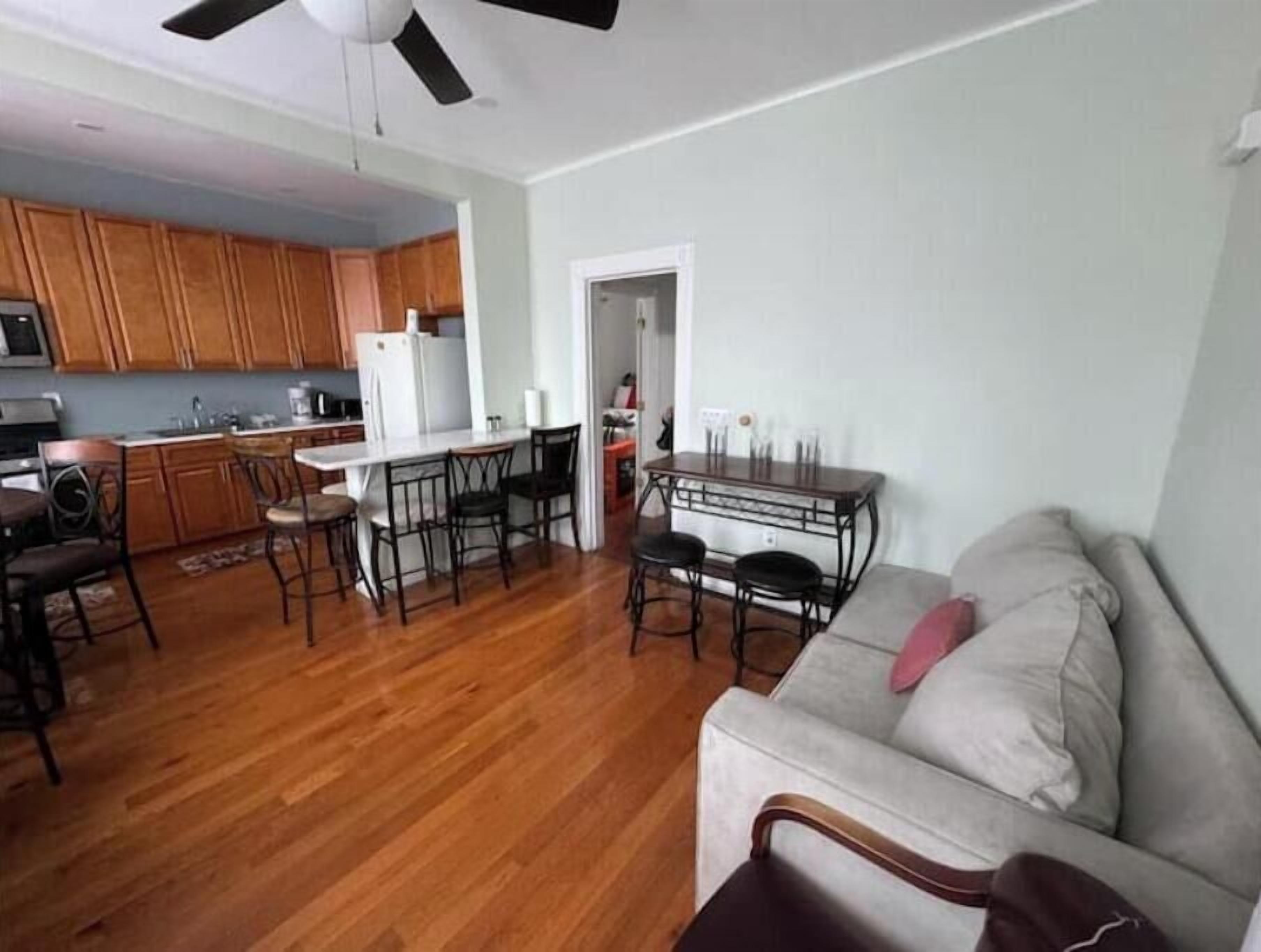 A spacious living room with a wooden floor, a grey sofa, and a dining area with a table and chairs.