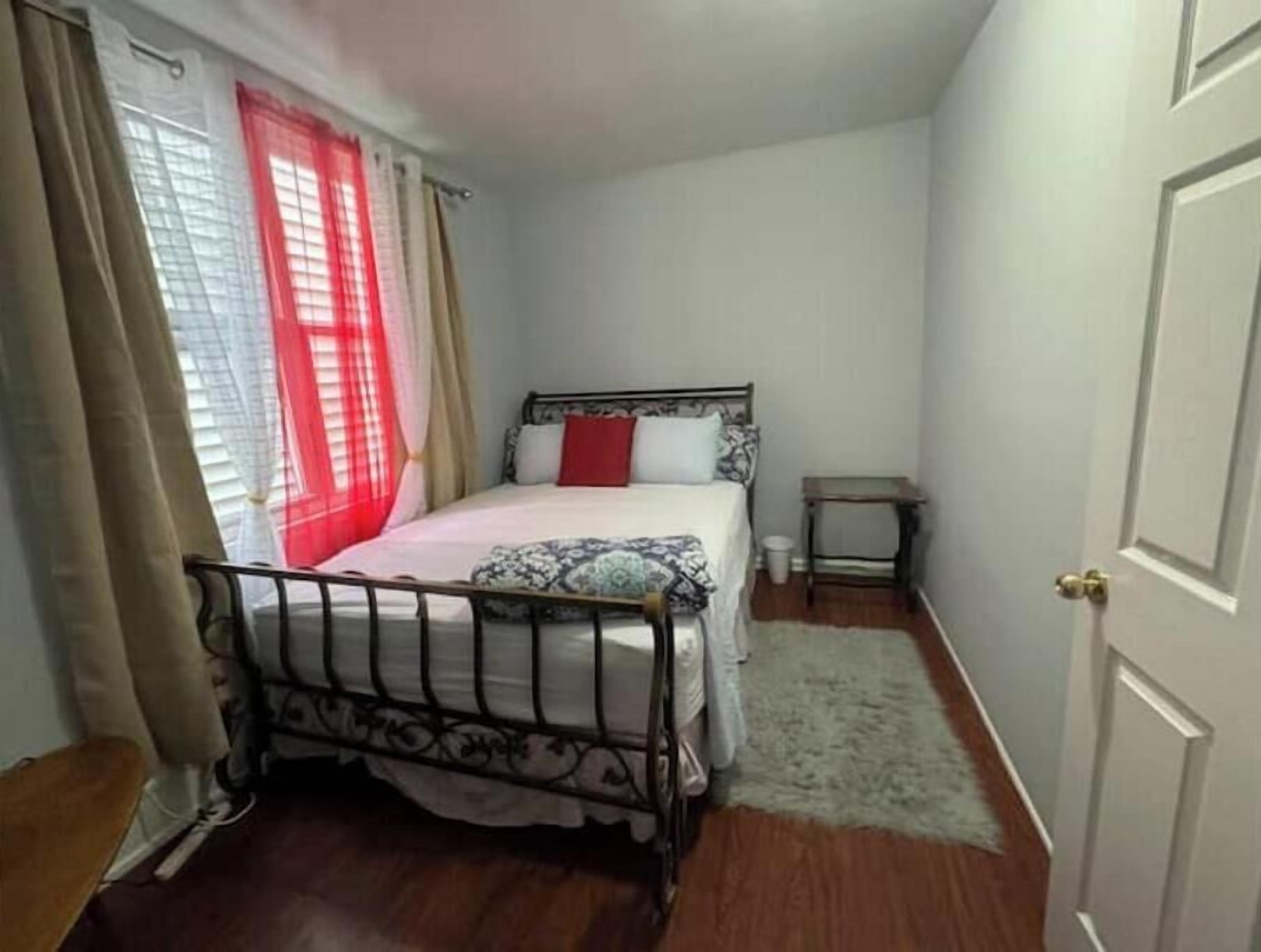 Un dormitorio pequeño y ordenado con una cama individual, una mesita de noche y una ventana con cortinas.