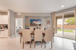 A dining area with a table and chairs, a kitchen in the background, and a painting of Las Vegas.