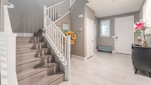 Eine Treppe mit weißen Geländern führt zu einer Empfangsebene, einer Bank und einer Tür.