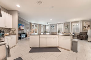 A spacious kitchen with a central island, a dining area, and a living space with a sofa and a chair.