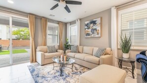 Ein Wohnzimmer mit einer Sofagarnitur, einem Couchtisch, einem Deckenventilator und einem großen Fenster mit Vorhängen.