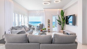 A modern living room with a sofa, armchairs, a coffee table, and a TV. There is a bookshelf and a plant.