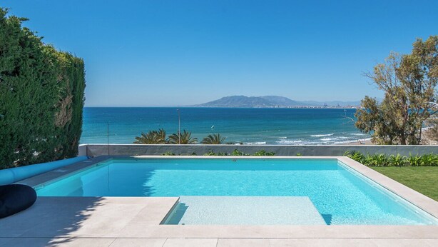 A swimming pool with a view of the ocean and a distant mountain.
