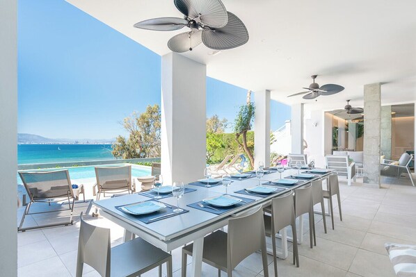 A dining area with a view of the ocean, a pool, and a beach.