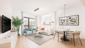Een moderne woonkamer met een bank, salontafel en stoelen. Er is een televisie aan de muur bevestigd, een potplant en kunst aan de wand.