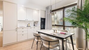 Eine moderne Küche mit weißen Schränken, einem Esstisch mit Stühlen und einem großen Fenster mit Vorhängen.