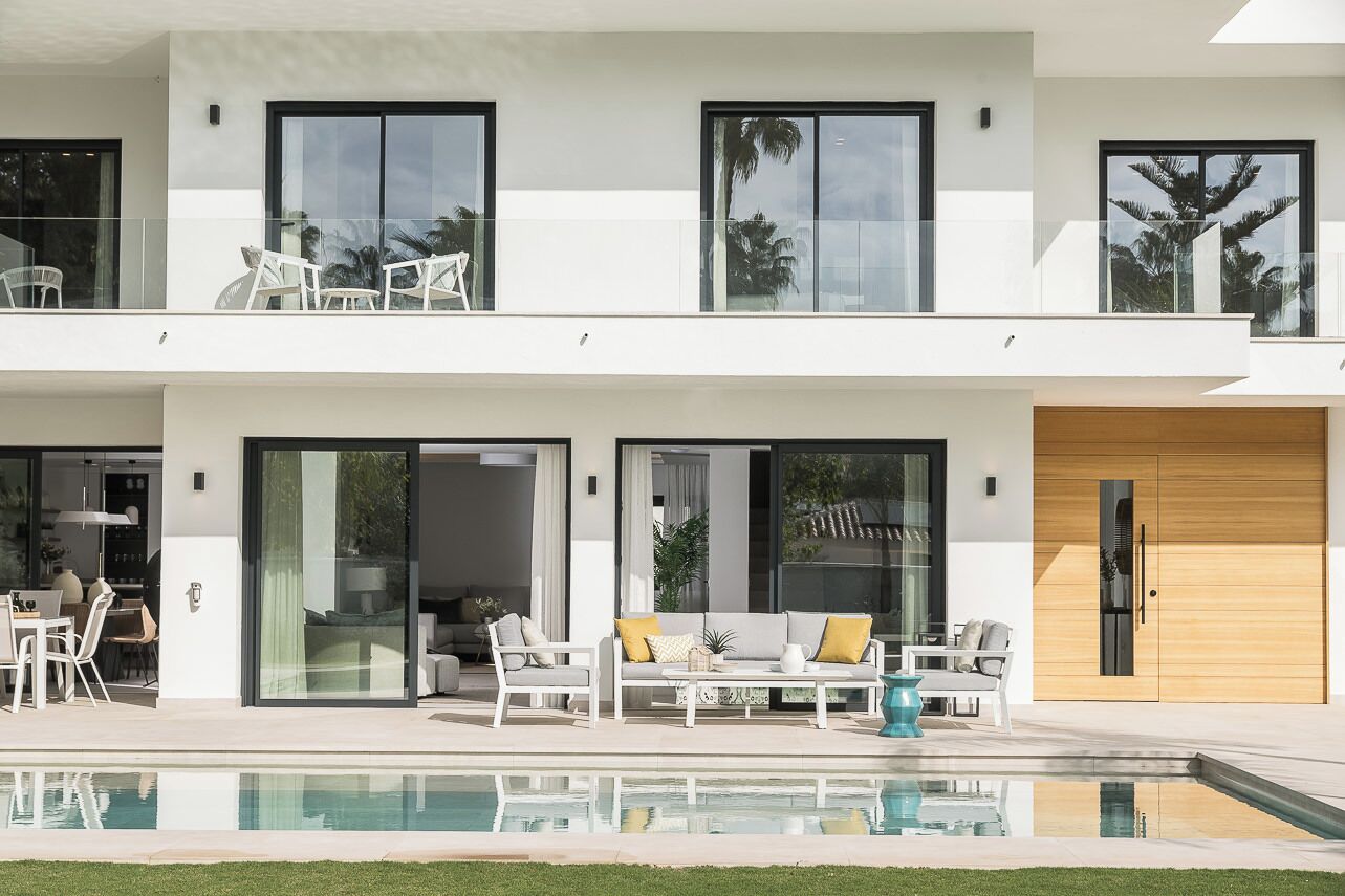 A modern two-story house with a swimming pool, large windows, and outdoor seating.