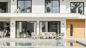 Una casa moderna de dos pisos con piscina, ventanas amplias y mobiliario exterior.