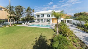 Una casa moderna de dos pisos con piscina, rodeada por un césped bien cuidado y diversas plantas.