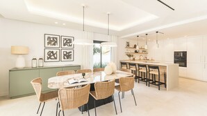 Un comedor moderno con una mesa redonda, sillas de mimbre, lámparas colgantes y vistas a la cocina.