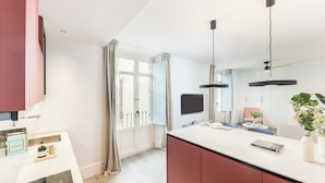 A modern kitchen with a large island, pendant lights, and a flat-screen TV.