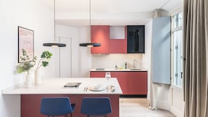 A modern kitchen with a central island, red and black cabinets, two pendant lights, and a dining area with blue chairs.