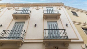 A building with three balconies, each with a black wrought iron railing and shutters.