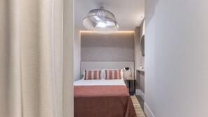 A modern hotel room with a large bed, a bedside table, a lamp, and a ceiling light fixture.