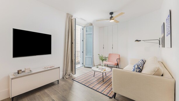 A modern living room with a flat-screen TV, a sofa, a coffee table, and a ceiling fan.