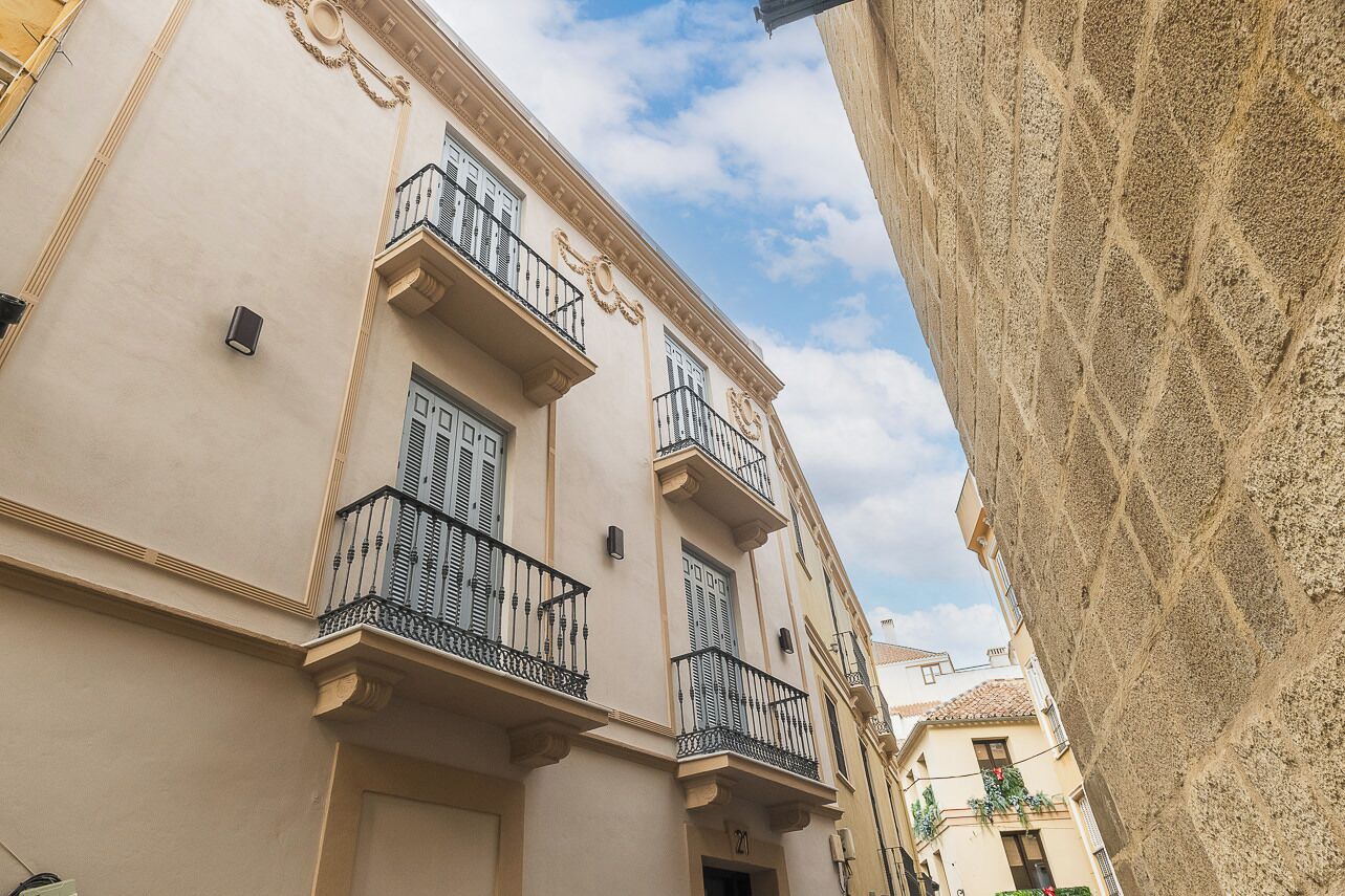 A narrow street with buildings featuring balconies and a stone wall.