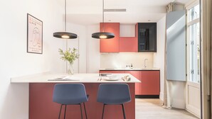 Une cuisine moderne dotée d’un îlot central, de deux tabourets de bar, d’un éclairage suspendu et d’une fenêtre avec des rideaux.