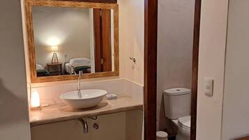 A bathroom with a large mirror, a white sink, a toilet, and a small trash bin.