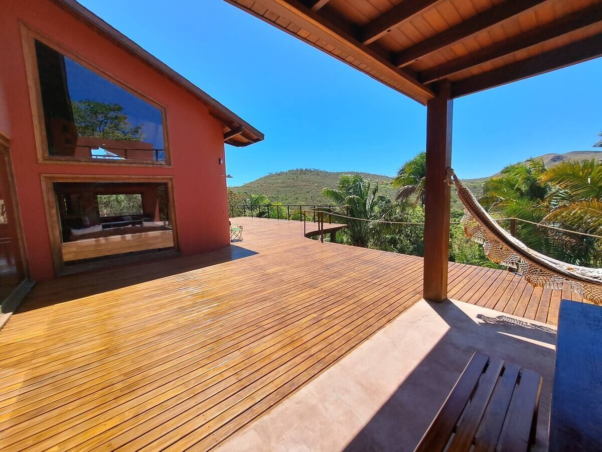 Une terrasse en bois avec un hamac, un bâtiment rouge et une vue sur des collines.
