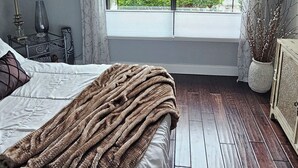 Ein Schlafzimmer mit großem Fenster, Deckenventilator, Bett mit brauner Decke und Nachttisch mit Lampe.