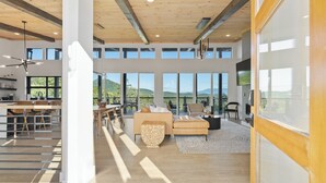 A spacious living area with a large window overlooking a scenic landscape, a wooden ceiling, and a modern kitchen in the background. - Smoky Vista / Hot Tub & Mountain Views (Sevierville)