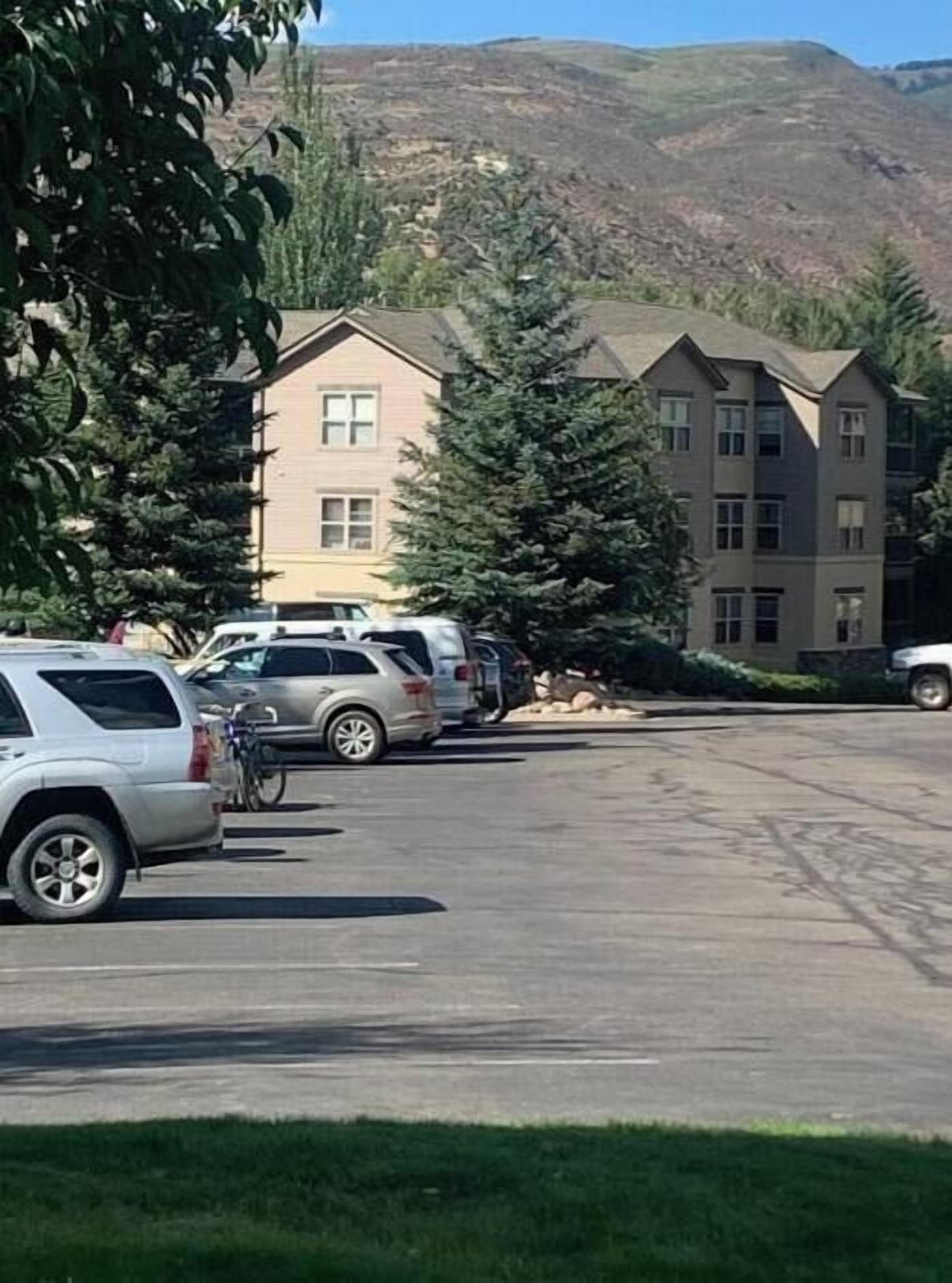 A parking lot with several cars and a bicycle. There are two multi-story buildings in the background with a mountainous landscape.