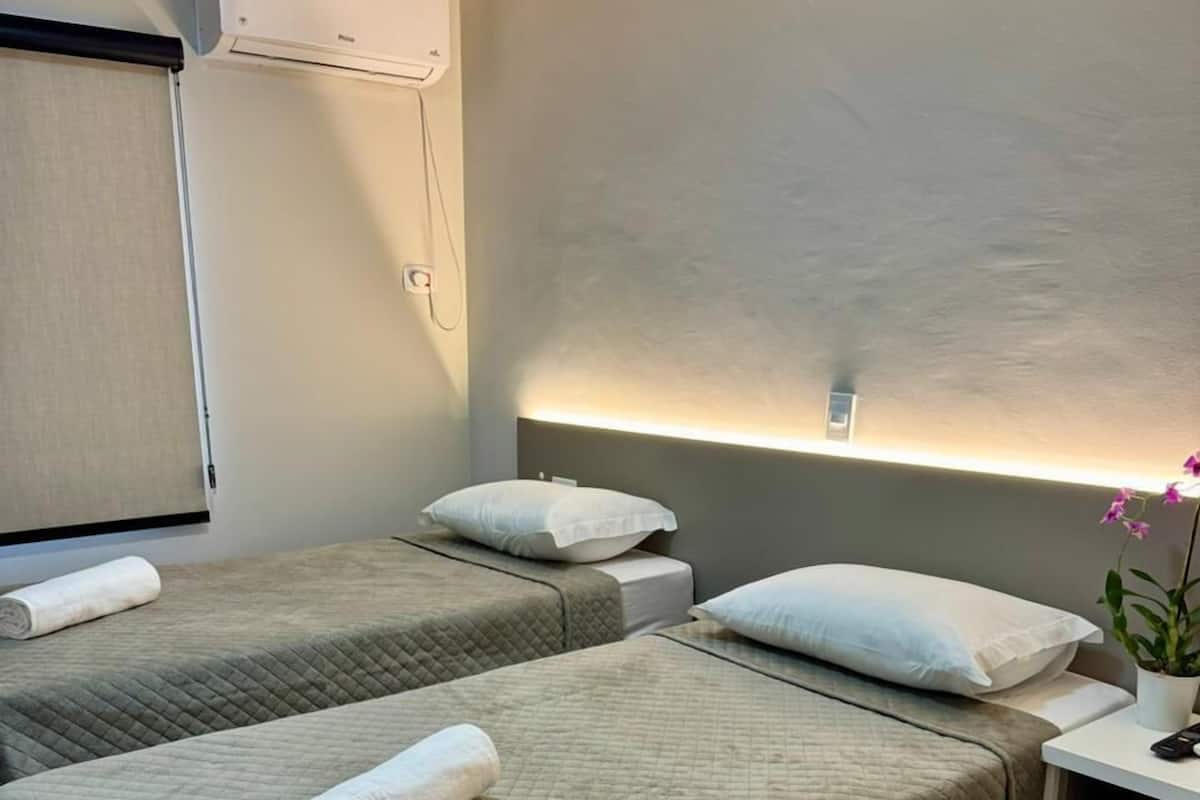 Habitación de hotel con dos camas, una mesita de noche con lámpara y un escritorio pequeño con silla.