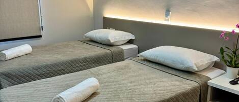 A hotel room with two beds, a bedside table with a lamp, and a small desk with a chair.